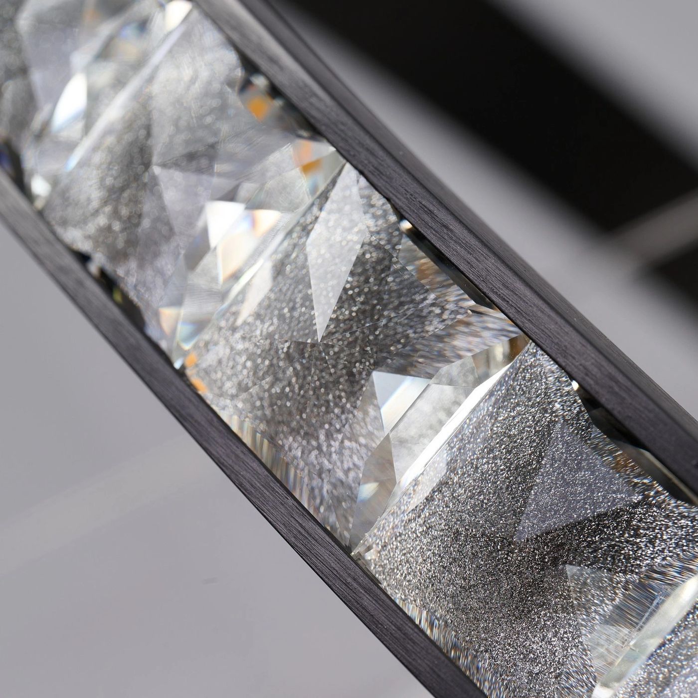 Czarna lampa wisząca Azalea z 1xLED 30W, z bliska ukazująca efektowne, diamentowe wzory kryształowego klosza, który odbija światło. Lampa ma prostą, nowoczesną konstrukcję z metalowym detalem.