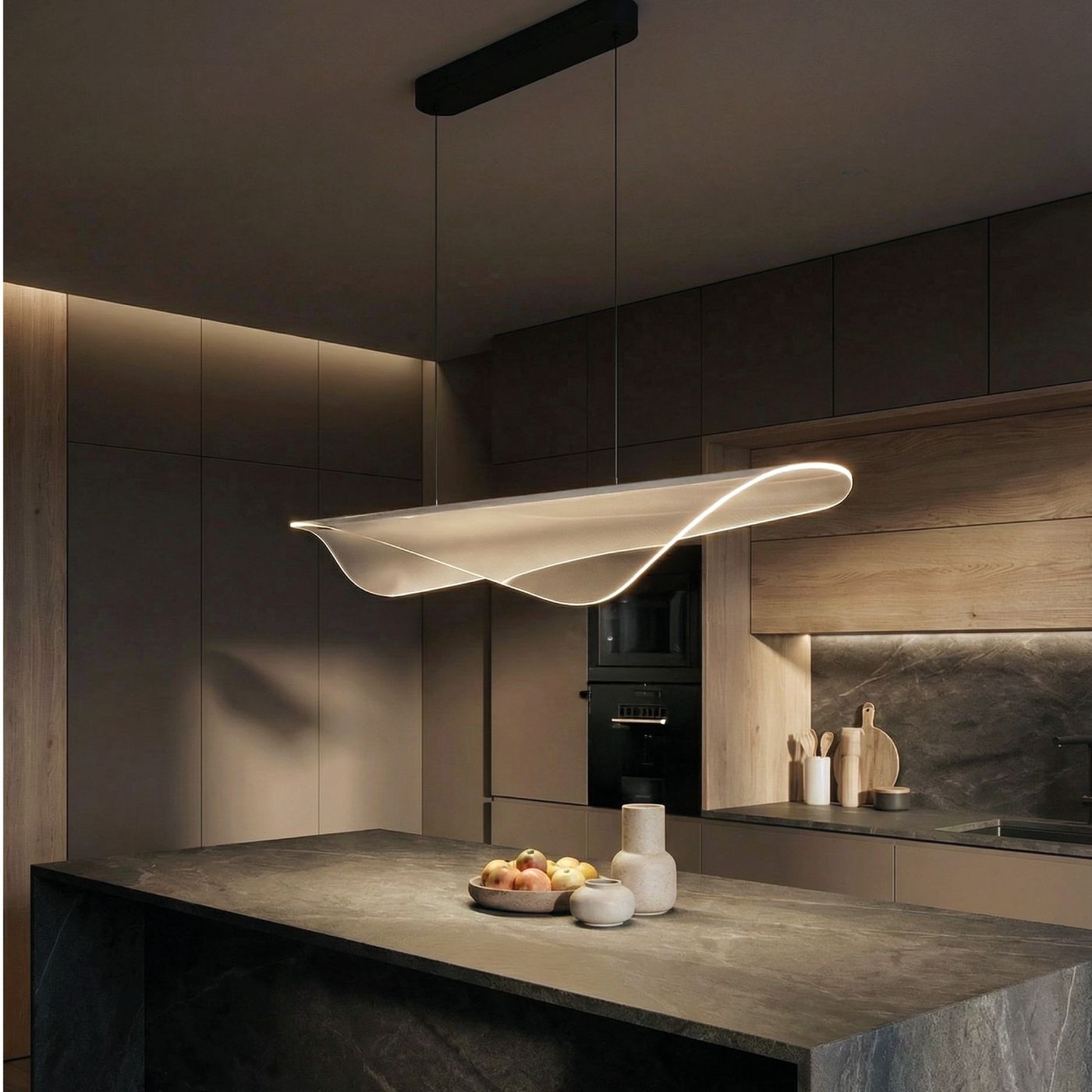 Lampa wisząca Manta 1xLED 38W w kolorze czarnym, o opływowym kształcie, zawieszona nad ciemnym blatem kuchennym. W tle widoczne drewniane elementy zabudowy kuchennej oraz akcesoria. Włączona, emitująca ciepłe światło.