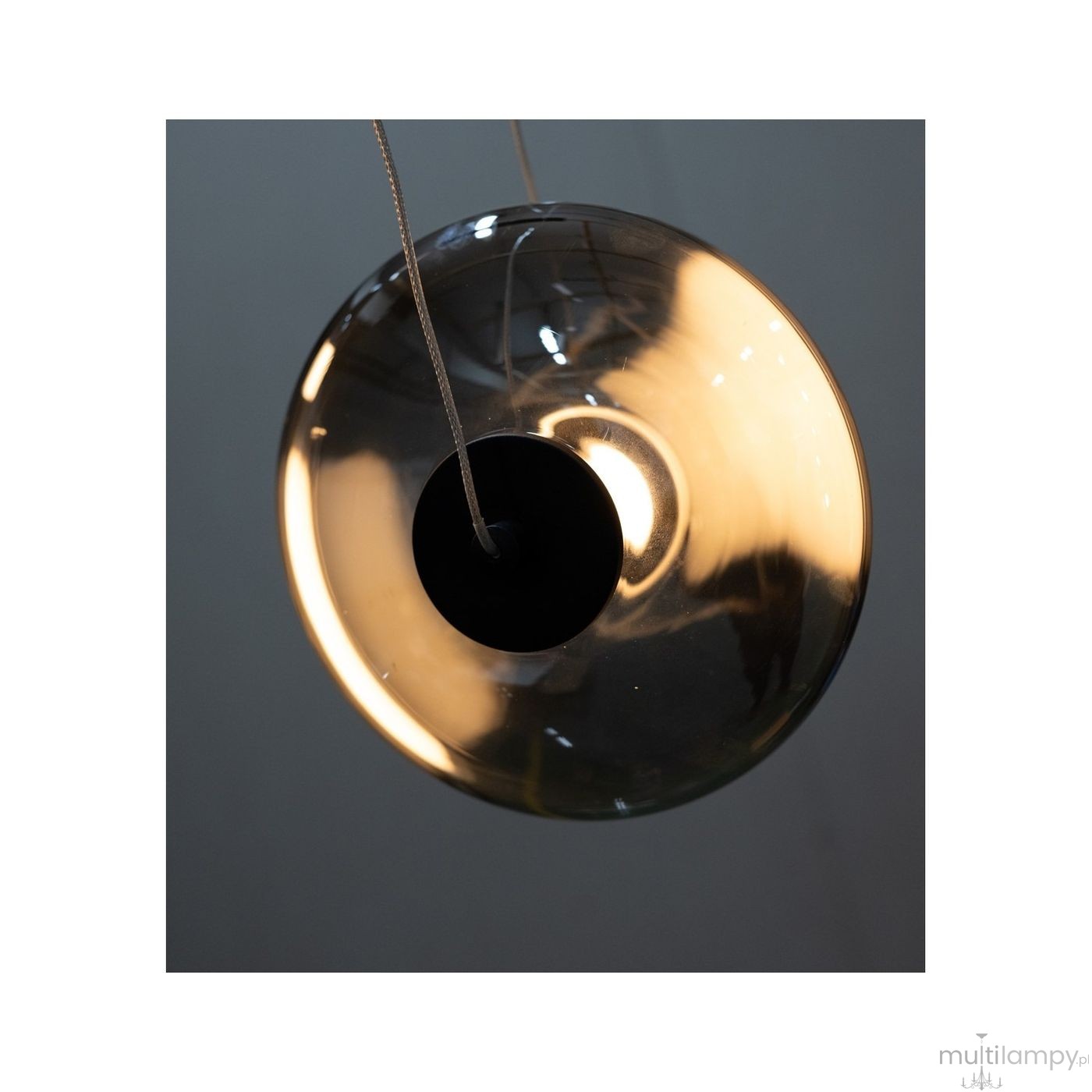Lampa wisząca Andora z jedną żarówką LED 12W, o złotej bursztynowej szklanej kloszu w kształcie okręgu. Widoczny czarny element mocujący i kabel zawieszenia. Ujęcie z bliska, ukazujące detale wzornictwa i źródło światła.