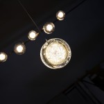 Złota lampa wisząca Euforia D13 z 1xLED 6W, w kształcie okrągłego klosza, zawieszona na cienkim przewodzie. Klosz ma przezroczyste, teksturowane wykończenie, emitujące ciepłe światło, z kilkoma podobnymi lampami w tle.