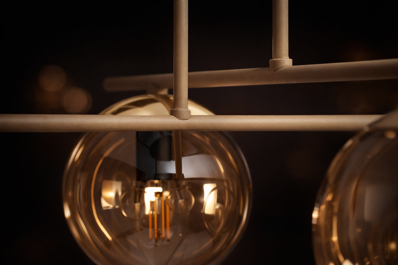 Beżowa lampa sufitowa Felix z czterema oprawami E14, z bursztynowymi kloszami w kształcie kul. Klosze umieszczone na metalowej konstrukcji w neutralnym kolorze. Widok z bliska, ukazujący detale mocowania i żarówek. Tło ciemne.