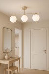 Lampa sufitowa Savia 3xE14 w kolorze beżowym i białym, z trzema okrągłymi kloszami, zamontowana na poziomej listwie, wisząca w jasnym wnętrzu z drewnianym stołem i lustrem.