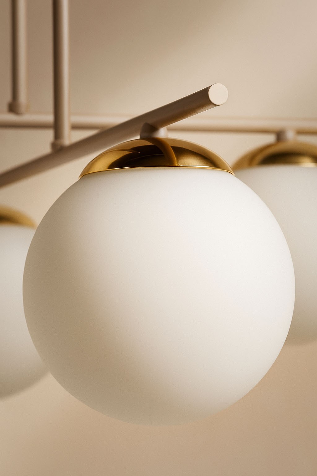 Lampa sufitowa Savia z czterema kulistymi kloszami w kolorze białym, z beżowym metalowym stelażem i złotą dekoracją na górze kloszy. Widok z bliska na detal klosza i elementy mocujące, zawieszona w prostym otoczeniu.