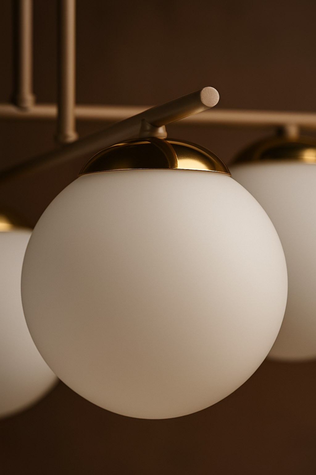 Beżowa lampa sufitowa Savia z sześcioma oprawami na żarówki E14. Szklane klosze w kształcie kul, matowe, z metalowymi złotymi detalami na górze. Lampa zamontowana na prostym stelażu, widok zbliżony na detal klosza.