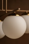 Beżowa lampa sufitowa Savia z sześcioma oprawami na żarówki E14. Szklane klosze w kształcie kul, matowe, z metalowymi złotymi detalami na górze. Lampa zamontowana na prostym stelażu, widok zbliżony na detal klosza.