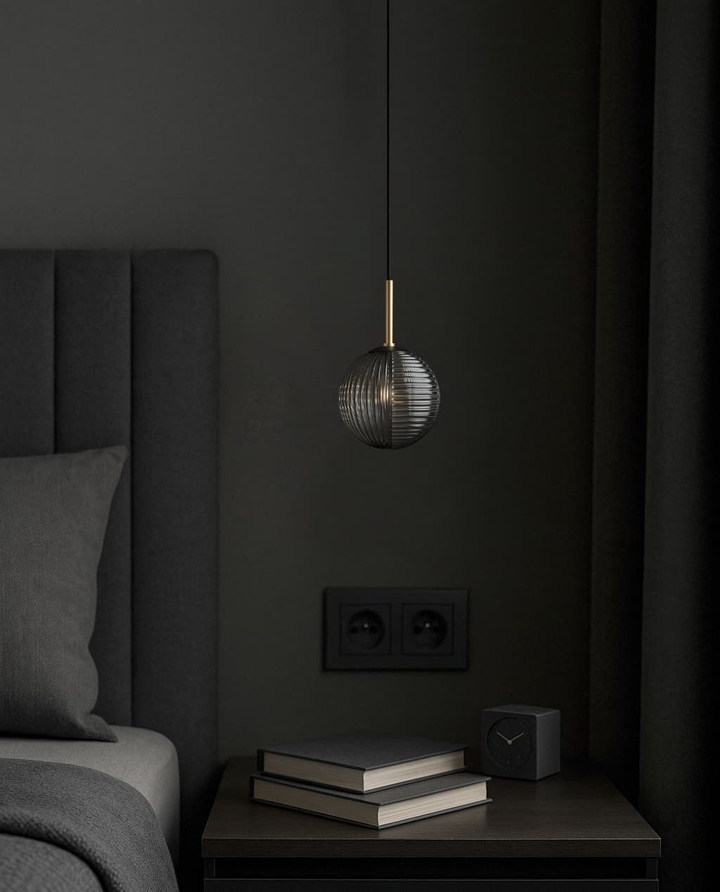 Lampa wisząca Fado 1xG9 w kolorze czarnym i grafitowym, z okrągłym kloszem z żłobieniami oraz złotym detalem u góry. Zawieszona na cienkim przewodzie, umieszczona nad stolikiem nocnym z książkami w nowoczesnej sypialni.