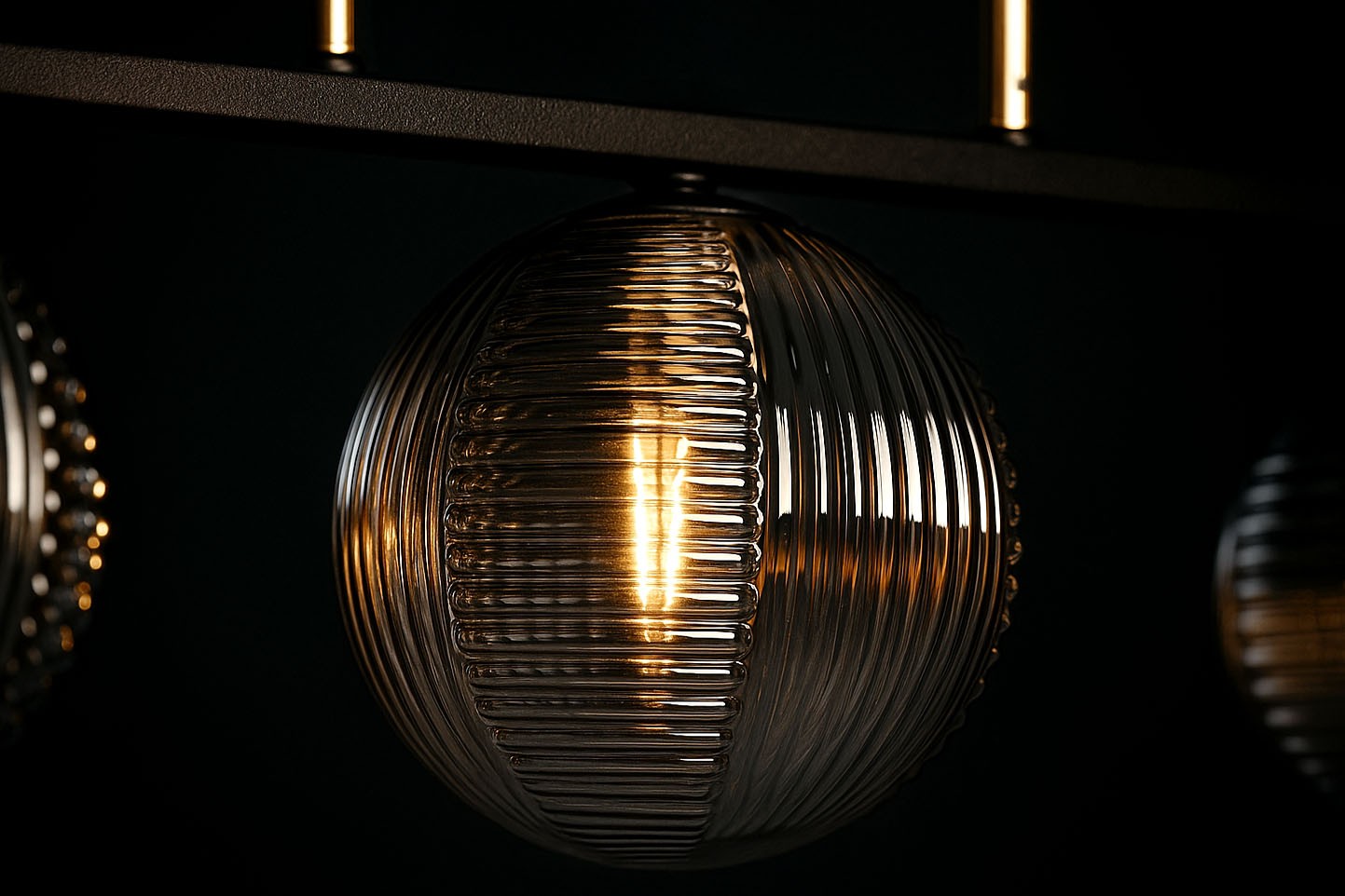 Lampa wisząca Fado w kolorze czarnym i grafitowym z trzema żarówkami G9. Szklana kula z wyraźnymi żłobieniami, emitująca ciepłe światło. Ujęcie z bliska, skupiające się na detalu tekstury klosza.