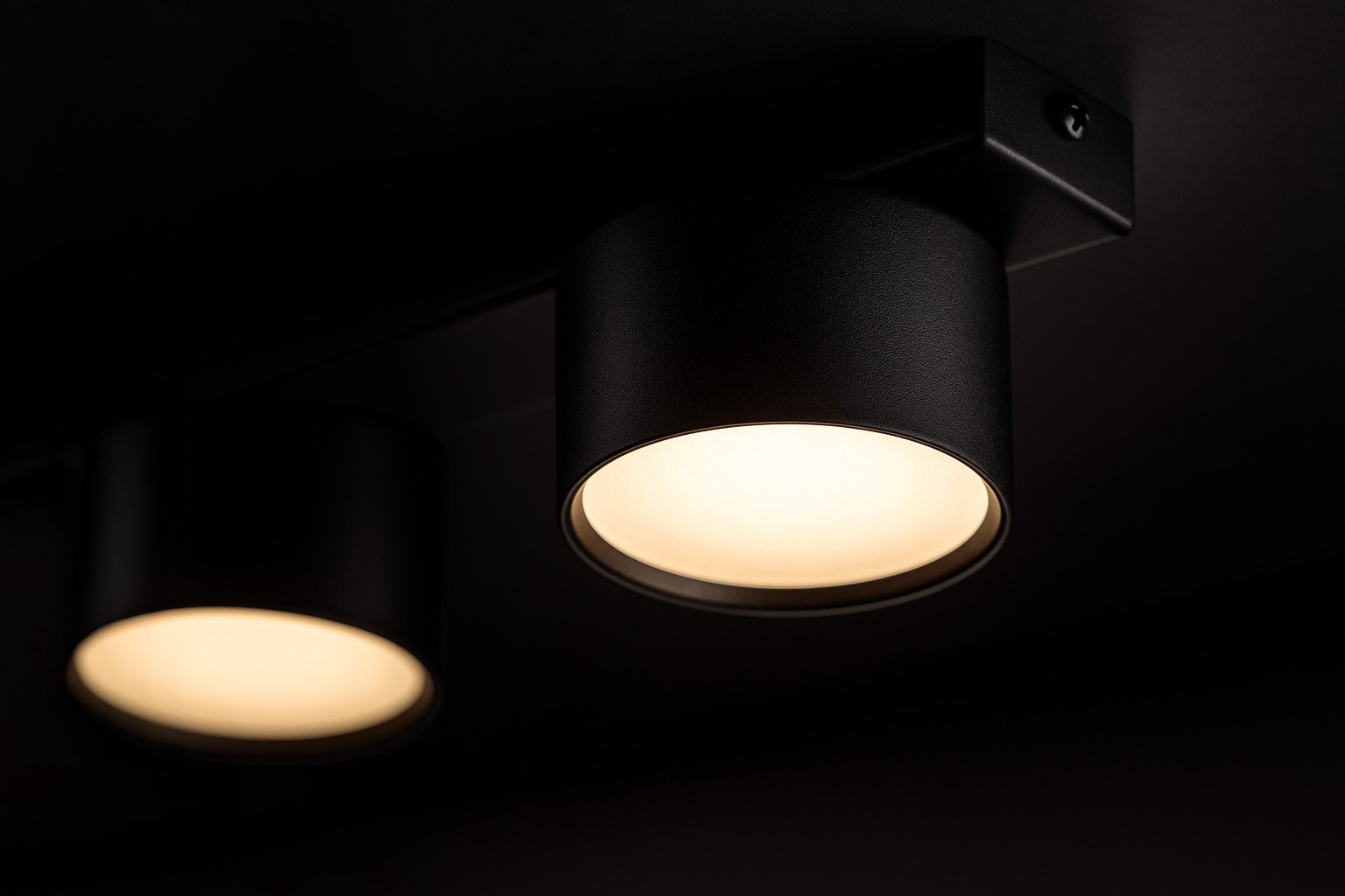 Cruz lampa sufitowa z pięcioma oprawami GX53 w kolorze czarnym. Ujęcie z boku, ukazujące okrągłe klosze z matowym wykończeniem i emitujące ciepłe światło. Lampa zamontowana na prostokątnej podstawie, na ciemnym tle.