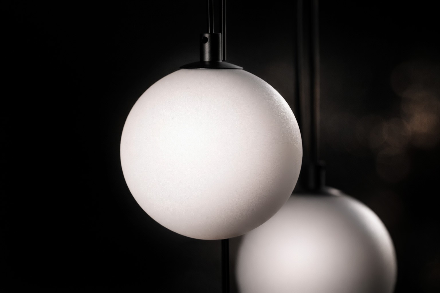 Lampa wisząca Aspen z ośmioma oprawami G9, w kolorze czarnym i białym. Okrągłe, matowe klosze w kształcie kul, zawieszone na cienkich, czarnych linkach. Kąt ujęcia zbliżeniowy, ukazujący detal klosza i jego fakturę na ciemnym tle.