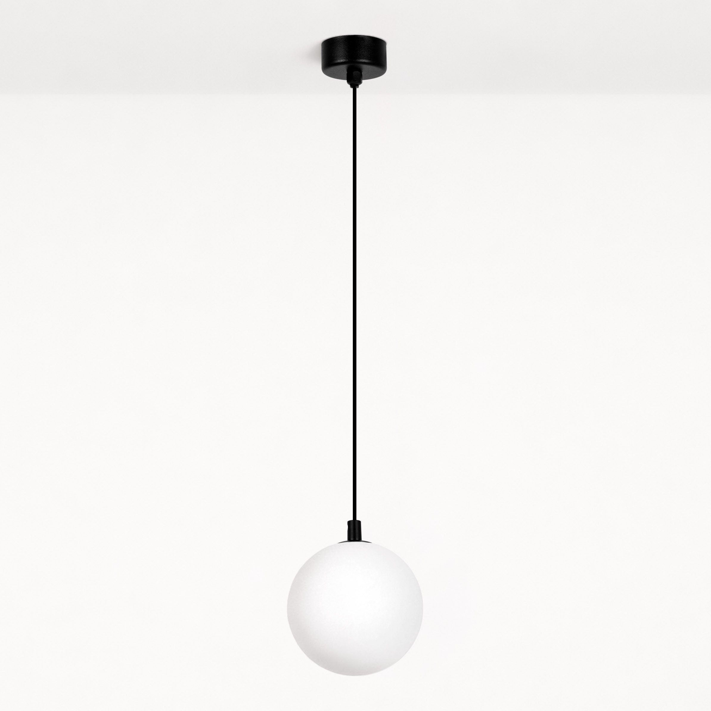Lampa wisząca Aspen z jednym źródłem światła G9, w kolorze czarnym z białym kloszem. Okrągły, matowy klosz zawieszony na cienkim, czarnym przewodzie. Prosta, nowoczesna forma, montowana do sufitu. Tło białe.