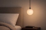 Lampa wisząca Aspen 1xG9 w kolorze czarnym z białym kloszem, w kształcie kuli. Powieszona nad nocnym stolikiem, w otoczeniu poduszki i książki. Kąt ujęcia frontalny, zbliżenie na detal lampy. Tło w jasnych odcieniach.