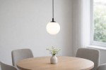 Lampa wisząca Aspen 1xG9 w kolorze czarnym i białym, o okrągłej, matowej klosze, zawieszona nad okrągłym drewnianym stołem. W tle widoczne są szare krzesła i okno, w którym widać zieleń na zewnątrz.