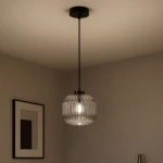 Lampa wisząca Campo D20 z czarnym metalowym mocowaniem i szklanym kloszem w grafitowym odcieniu, o okrągłym kształcie z teksturą prążków. Zawieszona na cienkim przewodzie, umieszczona w minimalistycznym wnętrzu.