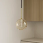 Lampa wisząca Galaxy z bursztynowym kloszem, zawieszona na czarnym przewodzie, z metalowym uchwytem w kolorze złotym. Kształt okrągły, z widoczną żarówką G9 wewnątrz. Prosta aranżacja, na tle jasnej ściany i drewnianych mebli.