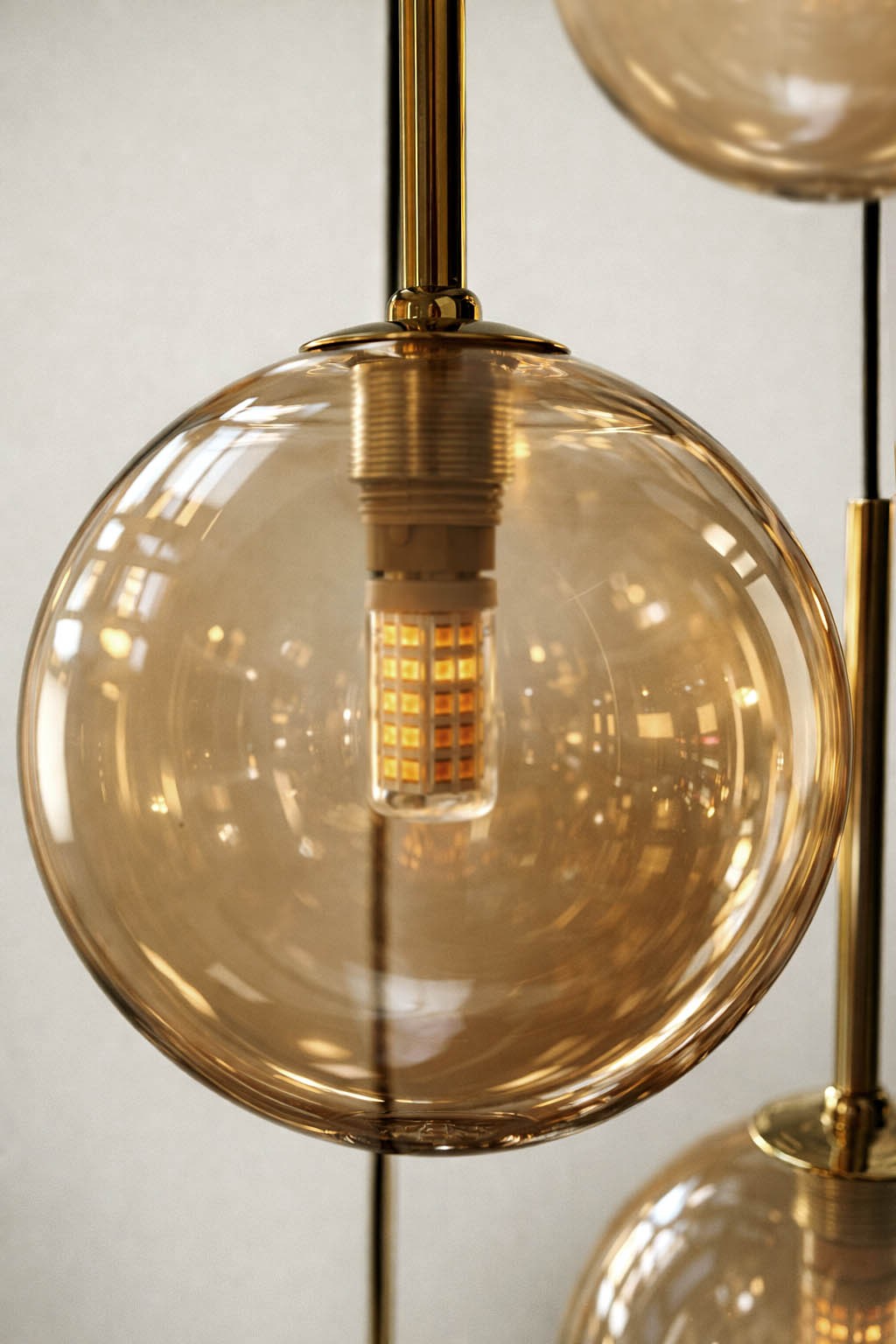 Lampa wisząca Galaxy w kolorze czarnym z bursztynowymi kulami, zawierająca osiem gniazd G9. Kula szklana z przezroczystym żarnikiem, metalowe elementy wykończenia w kolorze złotym, wisząca, zbliżenie na detal.