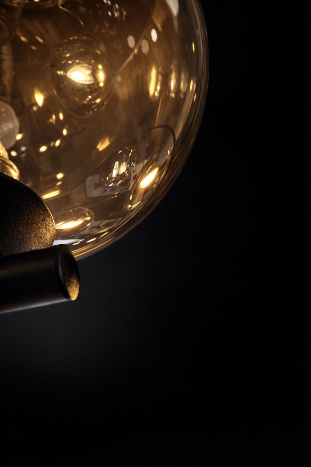 Kinkiet Galaxy w kolorze czarnym z bursztynową, szklaną kulą. Widok z boku, pokazujący detal mocowania oraz efektowne oświetlenie. Tło ciemne, podkreślające elegancki design lampy.