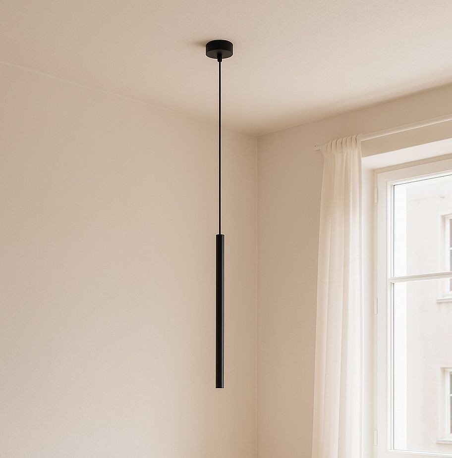 Lampa wisząca Gelato w kolorze czarnym, z pojedynczym źródłem światła G9. Prosty, cylindryczny kształt, zawieszona na cienkim kablu, w minimalistycznym wnętrzu z jasną ścianą i zasłoną.
