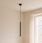 Lampa wisząca Gelato w kolorze czarnym, z pojedynczym źródłem światła G9. Prosty, cylindryczny kształt, zawieszona na cienkim kablu, w minimalistycznym wnętrzu z jasną ścianą i zasłoną.