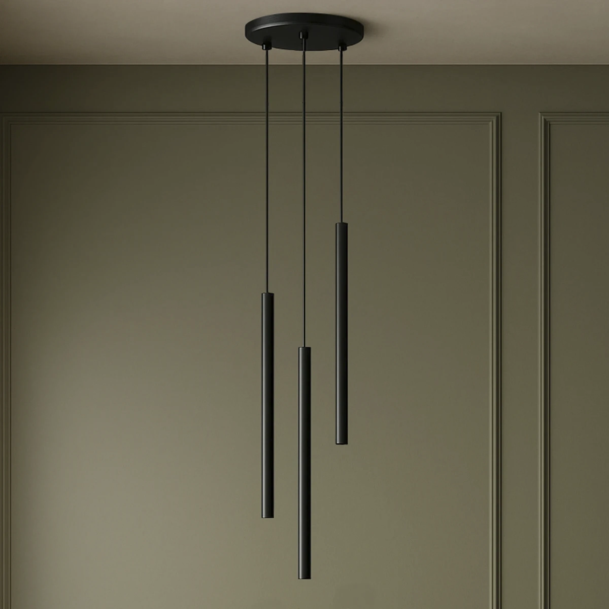Lampa wisząca Gelato 3xG9 w kolorze czarnym, składająca się z trzech długich cylindrycznych elementów zawieszonych na cienkich linkach. Montowana na okrągłej podstawie, idealna do nowoczesnych wnętrz. Tło w stonowanym odcieniu zieleni.