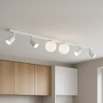 Lampa sufitowa Andi z białym wykończeniem, składająca się z czterech reflektorów GU10 i dwóch kul G9. Ujęcie z góry, pokazujące lampę zamontowaną na prostej listwie w nowoczesnym wnętrzu. W tle drewniane i białe szafki.