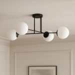 Czarna lampa sufitowa Savoy 4-punktowa K-4924 z metalową konstrukcją i czterema białymi, okrągłymi kloszami. Ujęcie z dołu, lampa zamontowana na suficie, w tle jasne ściany i delikatne detale architektoniczne.