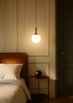 Lampa wisząca Faro D14 w kolorze czarnym, z okrągłym, białym kloszem, zawieszona na cienkim przewodzie. Widoczna w aranżacji sypialni obok łóżka z brązowym zagłówkiem i okrągłym, czarnym stolikiem nocnym.
