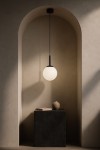 Czarna lampa wisząca Faro D16 z okrągłym kloszem z matowego szkła, zawieszona na cienkim kablu. Ujęcie frontalne, lampa umieszczona w architektonicznym wnęce, na tle jasnej, gładkiej ściany. Obok, na czarnym stole, widoczna ceramiczna waza i książka.