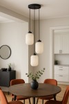 Lampa wisząca Vilar 3xE27 w kolorze czarnym i białym. Składa się z trzech cylindrycznych kloszy z fakturowanego szkła, zawieszonych na czarnych linkach. Umieszczona nad okrągłym drewnianym stołem we wnętrzu z brązowymi krzesłami i dekoracyjnym wazonem.