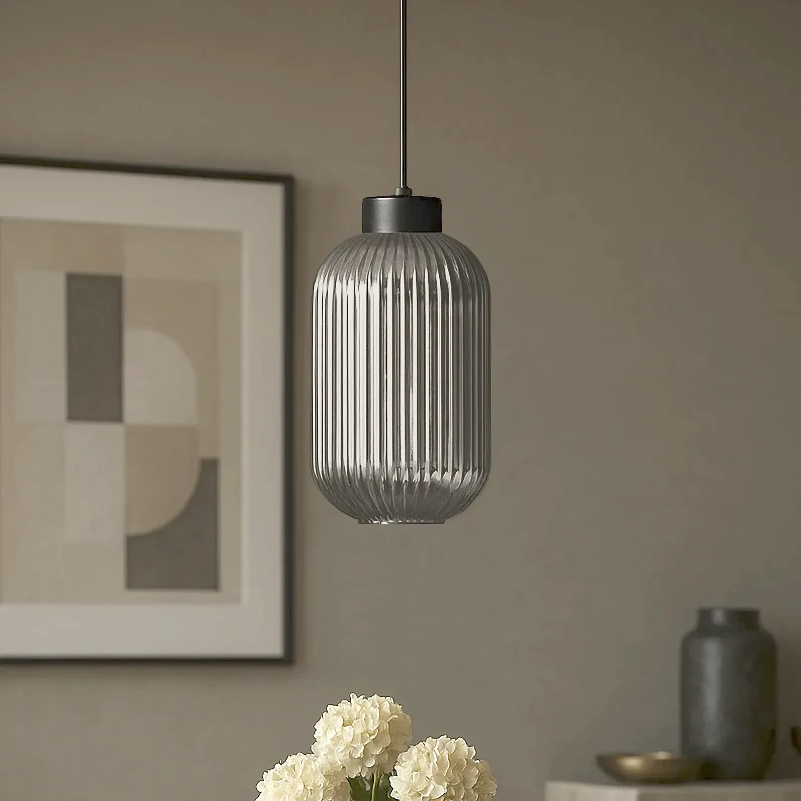 Lampa wisząca Silva D14 w kolorze czarnym i grafitowym, z przezroczystym kloszem w pionowe żłobienia. Zawieszona na cienkim przewodzie w nowoczesnym wnętrzu, w towarzystwie białych kwiatów i minimalistycznych dekoracji.