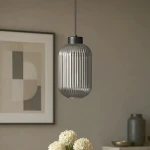 Lampa wisząca Silva D14 w kolorze czarnym i grafitowym, z przezroczystym kloszem w pionowe żłobienia. Zawieszona na cienkim przewodzie w nowoczesnym wnętrzu, w towarzystwie białych kwiatów i minimalistycznych dekoracji.