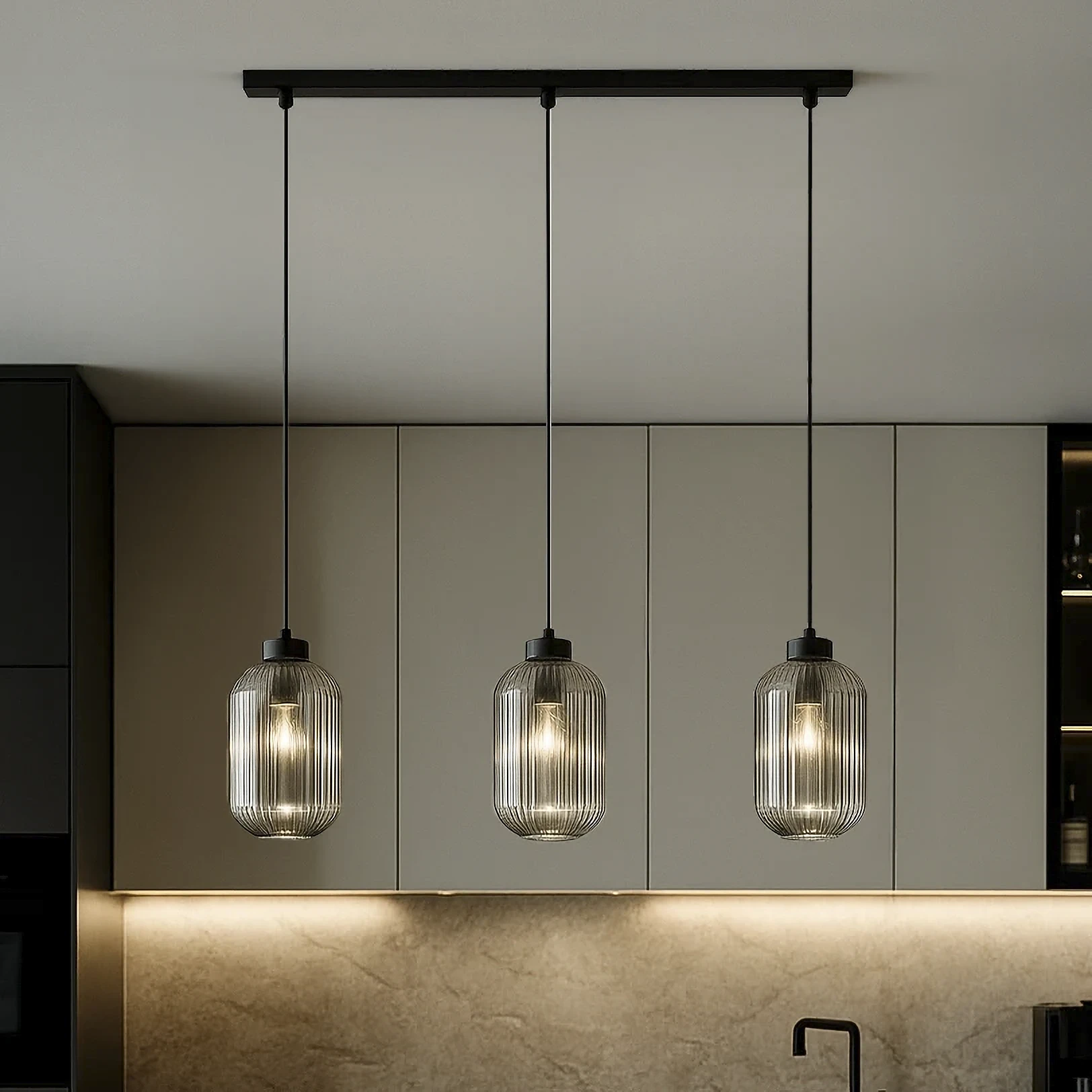 Lampa wisząca Silva 3xE27 w kolorze czarnym i grafitowym, z trzema szklanymi kloszami w formie cylindrów z przezroczystego szkła. Zawieszona na cienkich linkach, umieszczona nad blatem kuchennym, w nowoczesnym wnętrzu.