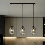 Lampa wisząca Silva 3xE27 w kolorze czarnym i grafitowym, z trzema szklanymi kloszami w formie cylindrów z przezroczystego szkła. Zawieszona na cienkich linkach, umieszczona nad blatem kuchennym, w nowoczesnym wnętrzu.
