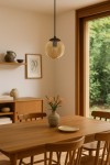Lampa wisząca Delta z żarówką E14, w czarnej oprawie z bursztynowym kloszem, zawieszona na cienkim kablu. Widok z góry, w tle drewniany stół z wazonem i kwiatami, w naturalnym wnętrzu z dużym oknem.