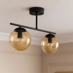 Lampa sufitowa Delta 2xE14 w kolorze czarnym z bursztynowymi kloszami. Zawieszona na metalowej rurze, z podwójnymi, okrągłymi kloszami, które mają przezroczyste wykończenie. Ujęcie z góry, pokazujące szczegóły konstrukcji i kształtu kloszy.