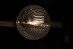 Lampa sufitowa Parma 2xG9 w kolorze czarnym z przezroczystym kloszem. Zbliżenie na okrągły klosz z teksturowanej szkła, zamontowany na prostokątnej podstawie, emitujący ciepłe światło. Tło ciemne, podkreślające detale lampy.