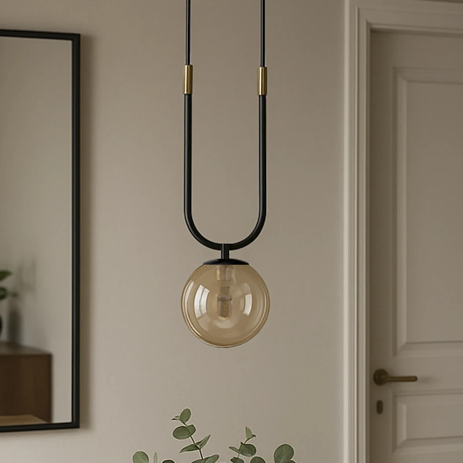 Lampa wisząca Goldi, czarna z bursztynowym kloszem, zawieszona na dwóch cienkich kablach. Kształt klosza kulisty, z widoczną żarówką G9. Tło neutralne, z elementami roślinnymi w dolnej części kadru.