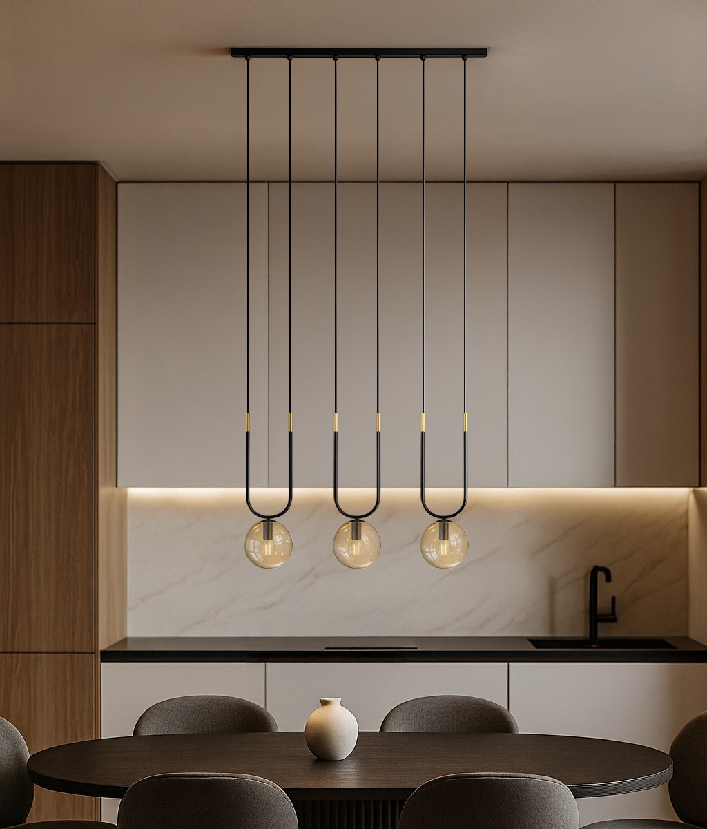 Lampa wisząca Goldi 3xG9 w kolorze czarnym z bursztynowymi kloszami, zawieszona na długich linkach z metalowymi detalami. Widoczna w nowoczesnej kuchni nad okrągłym stołem, z minimalistycznym tłem w odcieniach bieli i drewna.