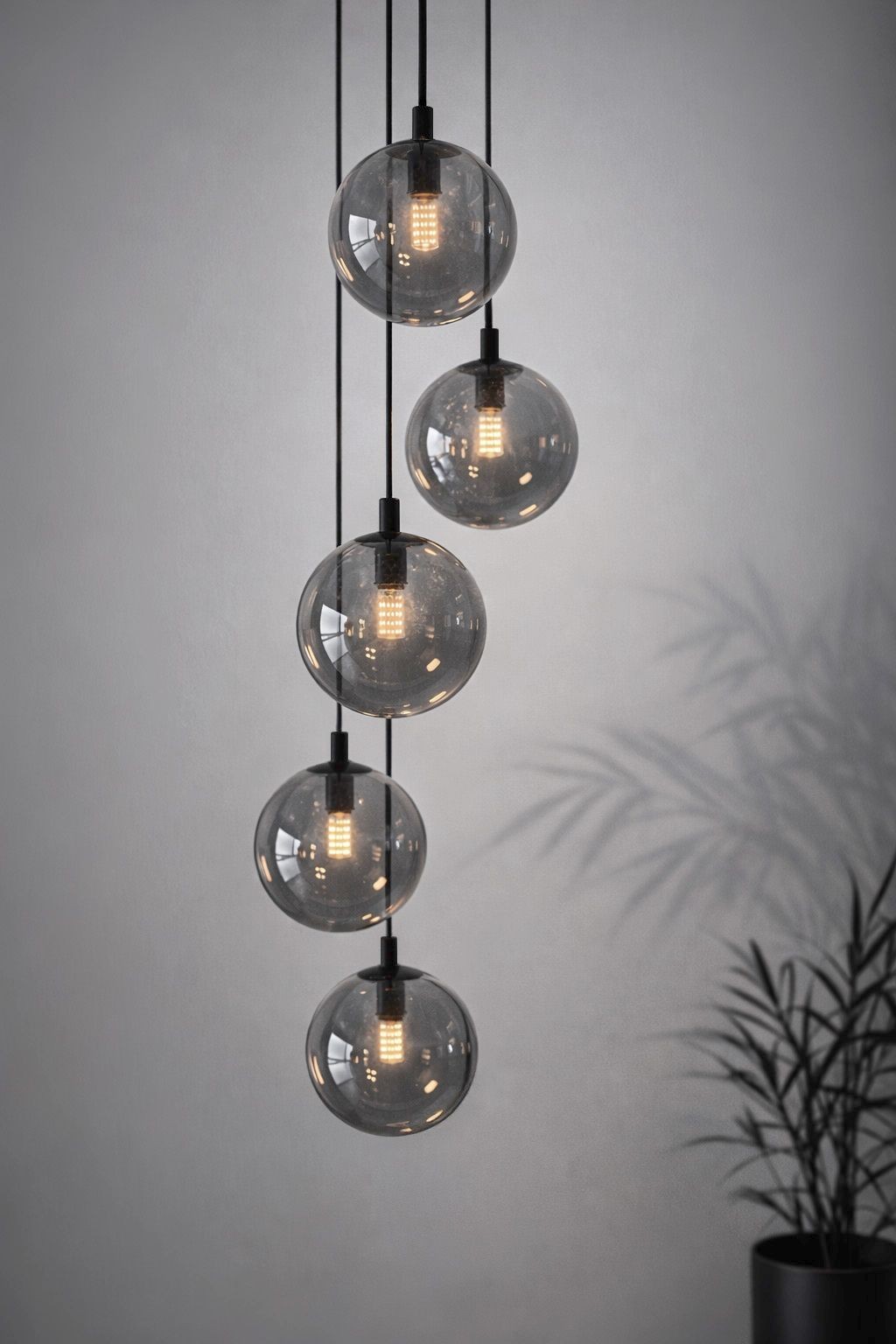 Lampa wisząca Dori w kolorze czarnym i grafitowym z pięcioma okrągłymi kloszami z przezroczystego szkła, zawieszona na czarnych przewodach. Klosze o wykończeniu w ciemnym tonie, emitują ciepłe światło.