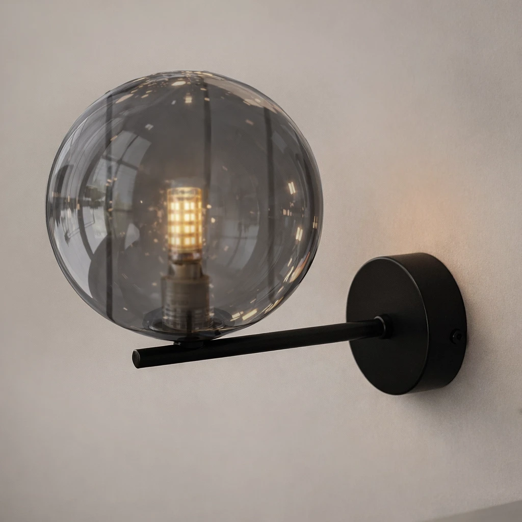 Kinkiet Dori z czarną/grafitową oprawą, z przezroczystą kulistą kloszem. Produkt montowany na ścianie, w zbliżeniu na źródło światła G9. Stylowy, minimalistyczny design, idealny do nowoczesnych wnętrz.