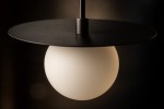Lampa wisząca Robin D18 w kolorze czarnym i białym, z okrągłym, matowym kloszem oraz płaskim, okrągłym daszkiem. Ujęcie z bliska, ukazujące detale konstrukcji oraz fakturę materiału. Wisi na cienkim przewodzie w ciemnym tle.