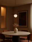 Lampa wisząca Robin D25 z czarnym metalowym daszkiem i białą, okrągłą kulą. Ujęcie z dołu, zawieszona nad okrągłym stołem z szarym blatem, otoczona brązowymi krzesłami. W tle widać delikatne oświetlenie oraz dekoracyjny obraz.