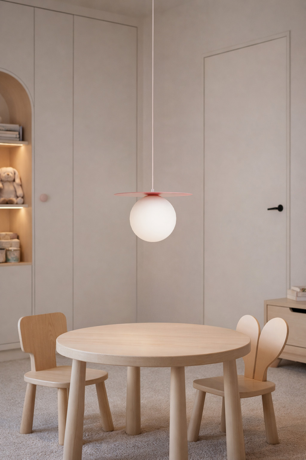 Lampa wisząca Robin D18 z jedną oprawą G9, w kolorze różowym i białym. Okrągła, matowa kula z różowym daszkiem, zawieszona na cienkim przewodzie. Umieszczona nad drewnianym stolikiem i krzesłami w jasnym wnętrzu.