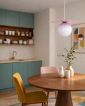 Lampa wisząca Robin D25 z różowym kloszem i białą kulą, zawieszona nad okrągłym drewnianym stołem. W tle widoczne zielone szafki kuchenne oraz dekoracyjne elementy na stole, w tym wazon z rośliną.