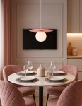 Lampa wisząca Robin D25 z różowym talerzem i białą kulą, zawieszona nad okrągłym stołem z białym marmurowym blatem. Otoczenie w pastelowych odcieniach, z różowym obiciem krzeseł i subtelnymi dekoracjami w tle.