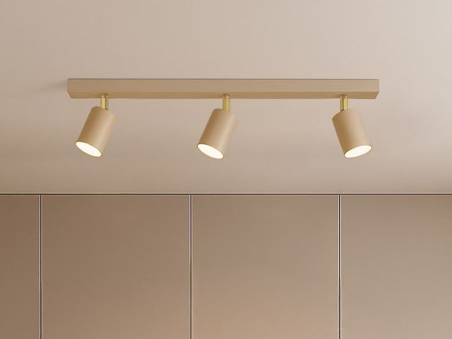 Beżowa lampa sufitowa typu spot z trzema ruchomymi oprawami na żarówki GU10. Zamontowana poziomo na prostokątnej podstawie, idealna do oświetlenia wnętrz. W tle gładkie, jasne ściany.