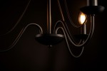 Czarny żyrandol Bartez 3-punktowy K-3990, widok z boku na eleganckie, zakrzywione ramiona i lampy. Materiał metalowy, matowa powierzchnia. Jedna żarówka włączona, emitująca ciepłe światło. Tło ciemne, podkreślające detal.