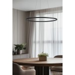 Lampa wisząca Apus w kolorze czarnym, o okrągłym kształcie, zawieszona na cienkich linkach. Wyposażona w 10 diod LED, umieszczona nad okrągłym stołem, otoczona jasnymi zasłonami i roślinnością w tle.