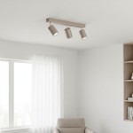 Lampa sufitowa Spoti, 3xGU10, w kolorze kaszmiru i złota. Ustawiona poziomo, z trzema cylindrycznymi kloszami, skierowanymi w dół. Tło jasne, minimalistyczne wnętrze z białymi zasłonami i półką na książki.