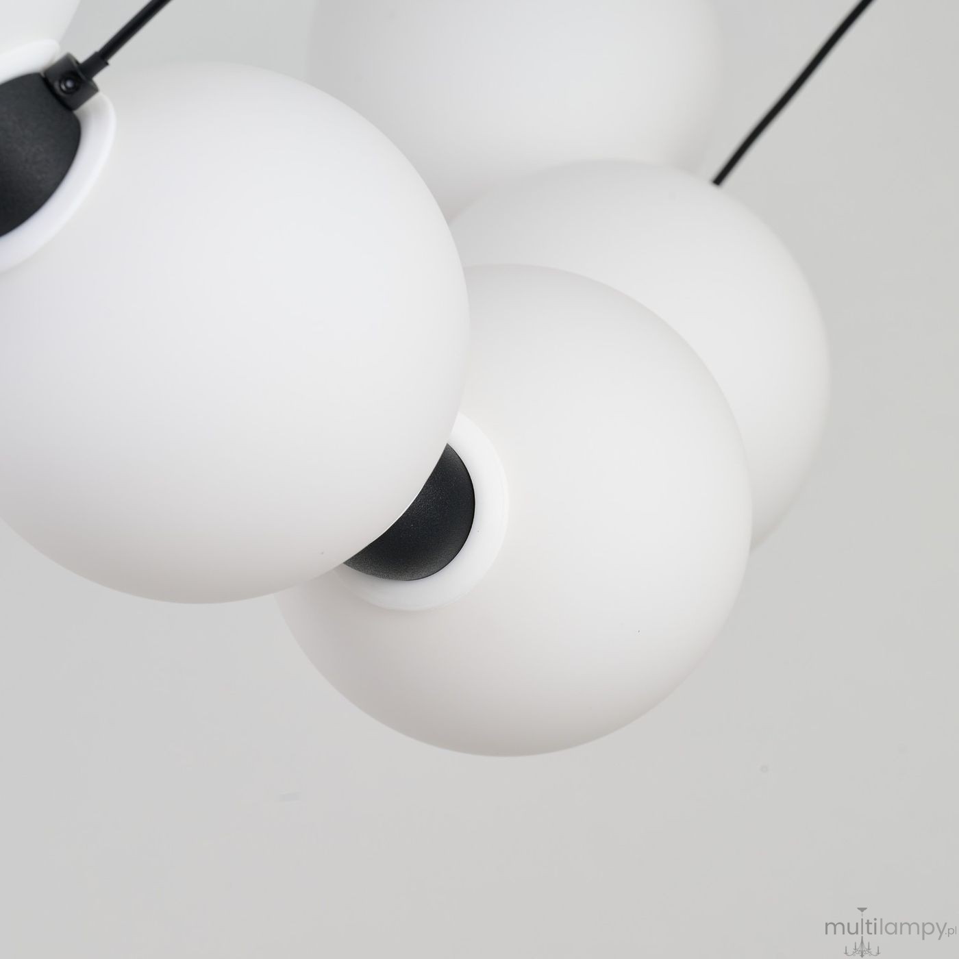 Lampa wisząca Perla z 15 kulistymi kloszami w białym matowym kolorze, zawieszona na czarnych linkach. Klosze mają czarne mocowania i są umieszczone blisko siebie, tworząc nowoczesny, minimalistyczny design.