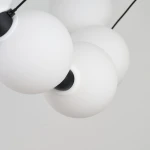 Lampa wisząca Perla z 15 kulistymi kloszami w białym matowym kolorze, zawieszona na czarnych linkach. Klosze mają czarne mocowania i są umieszczone blisko siebie, tworząc nowoczesny, minimalistyczny design.